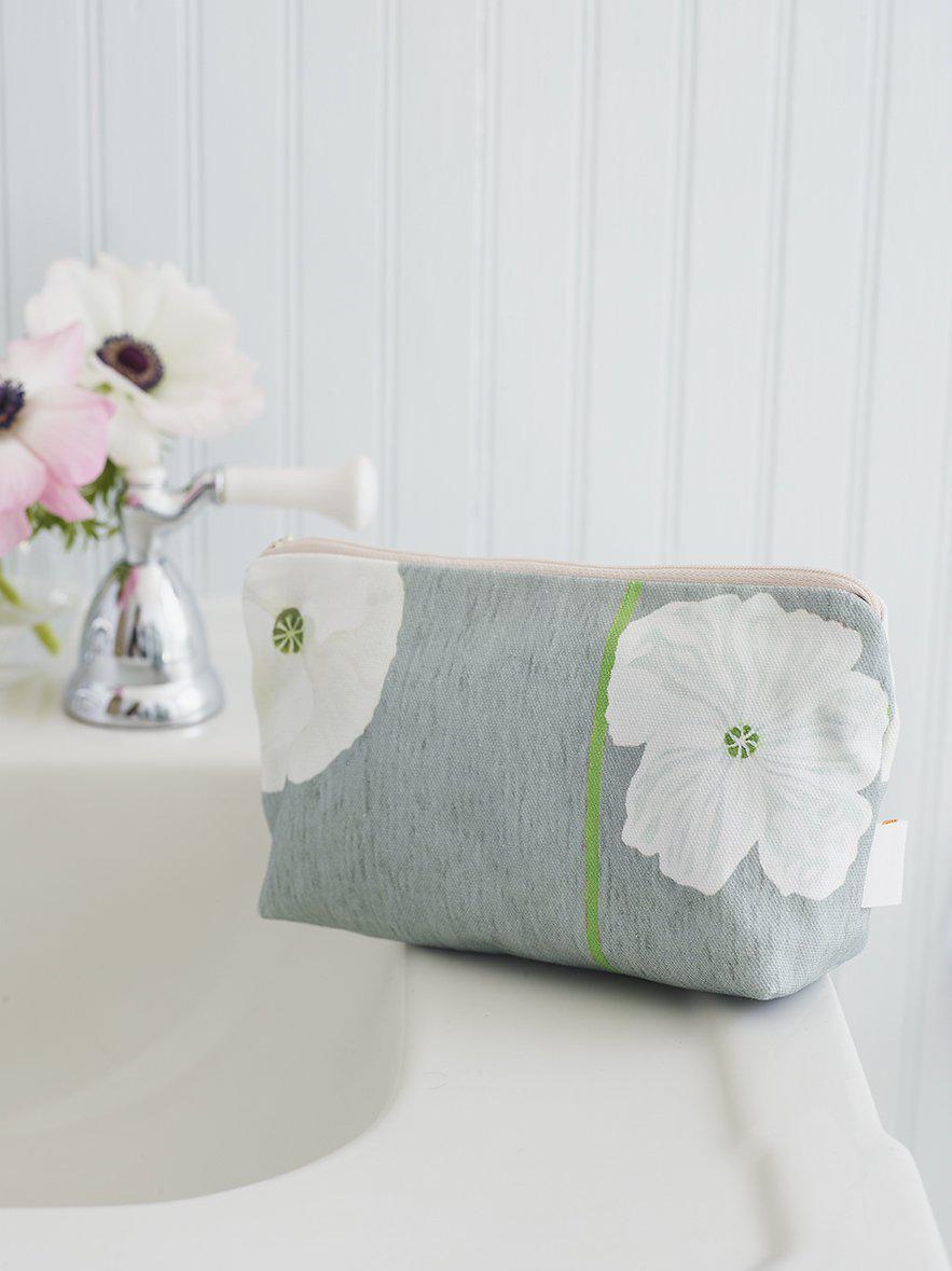 Gray makeup bag with white poppy flowers on bathroom sink near silver faucet and white paneled wall