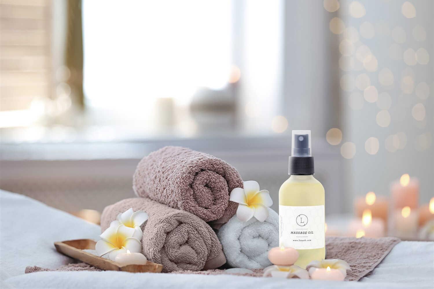 Massage oil bottle with rolled towels, frangipani flowers, and lit candles in spa setting