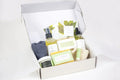 Open white gift box with men's bath and body care products including massage oil, soaps, foot cream, lip balm, and towel