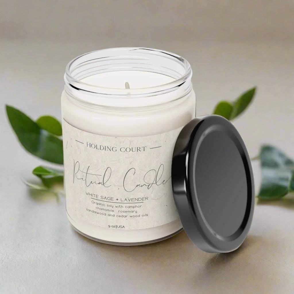 Holding Court Ritual Candle with white sage and lavender scent in clear glass jar with black lid
