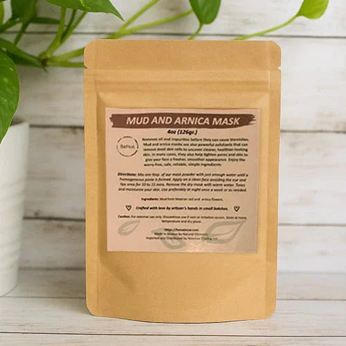 Mud and Arnica Mask in eco-friendly packaging on white wooden surface, greenery beside. Qu!rk Boutique skincare product.