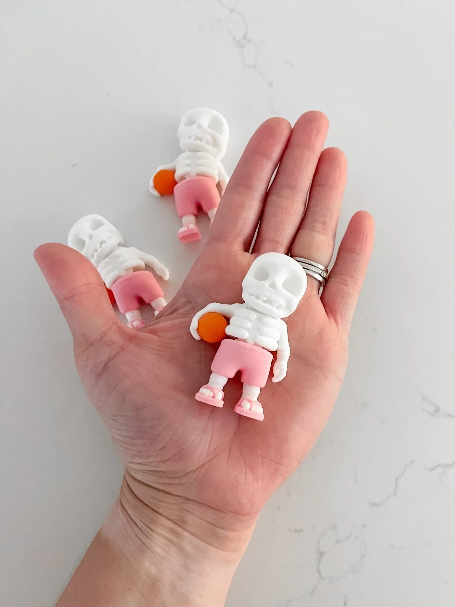 Hand holding a small white skeleton figure in pink shorts with orange accessory, quirky gift toy