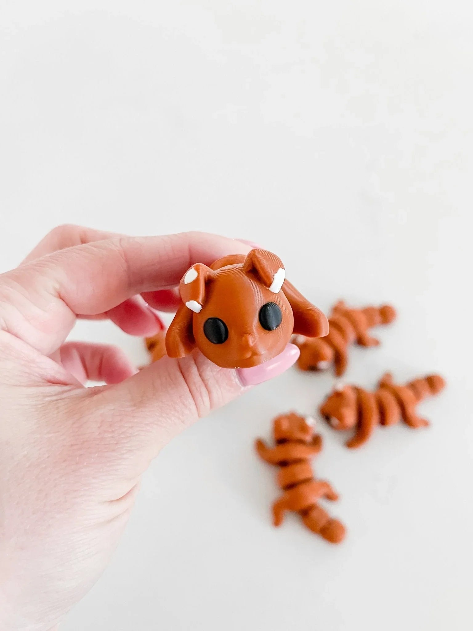 Hand holding a small brown baby critter toy with black eyes, others on white background