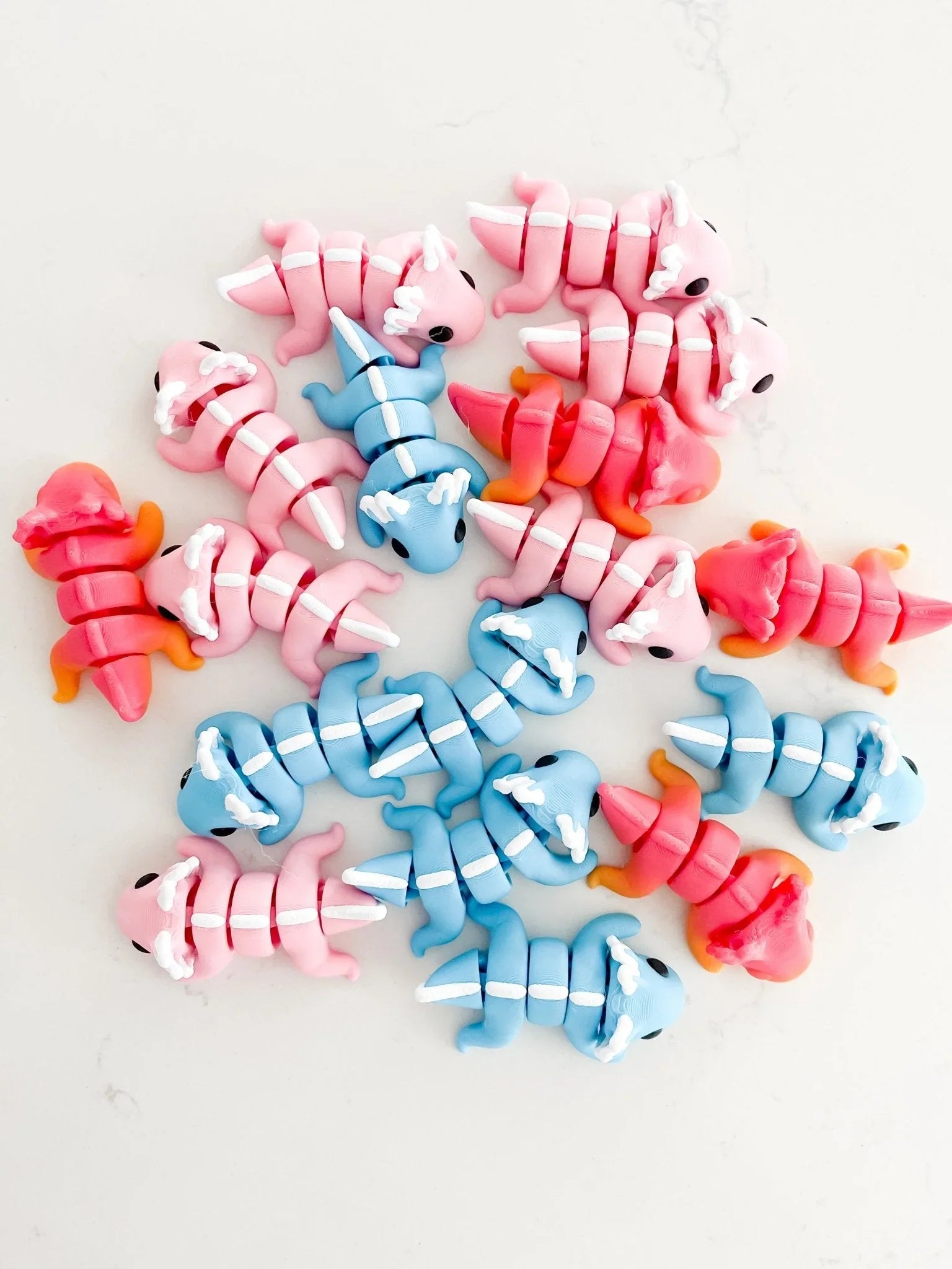 Assorted pastel pink, blue, and red axolotl baby critter toys on white background at Qu!rk Boutique