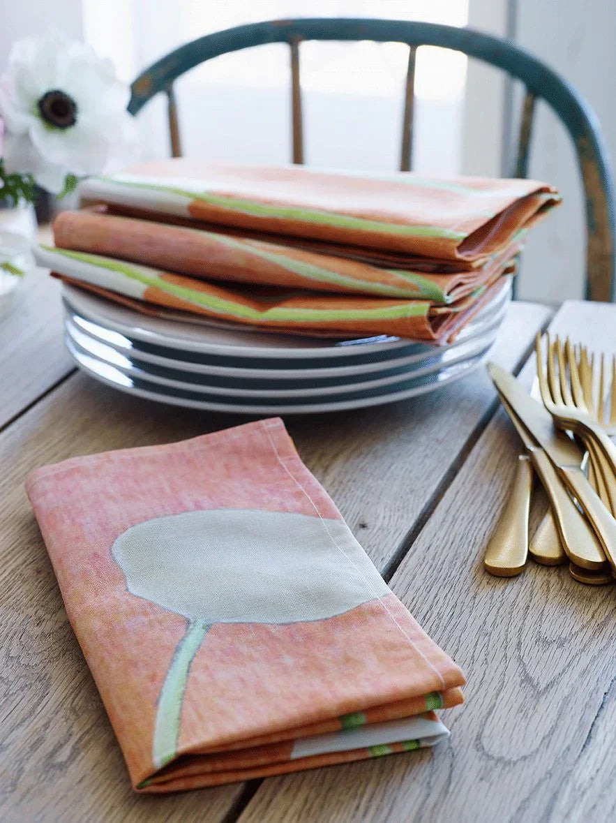 Stack of cream floral patterned orange cloth napkins on white plates with gold cutlery on wooden table