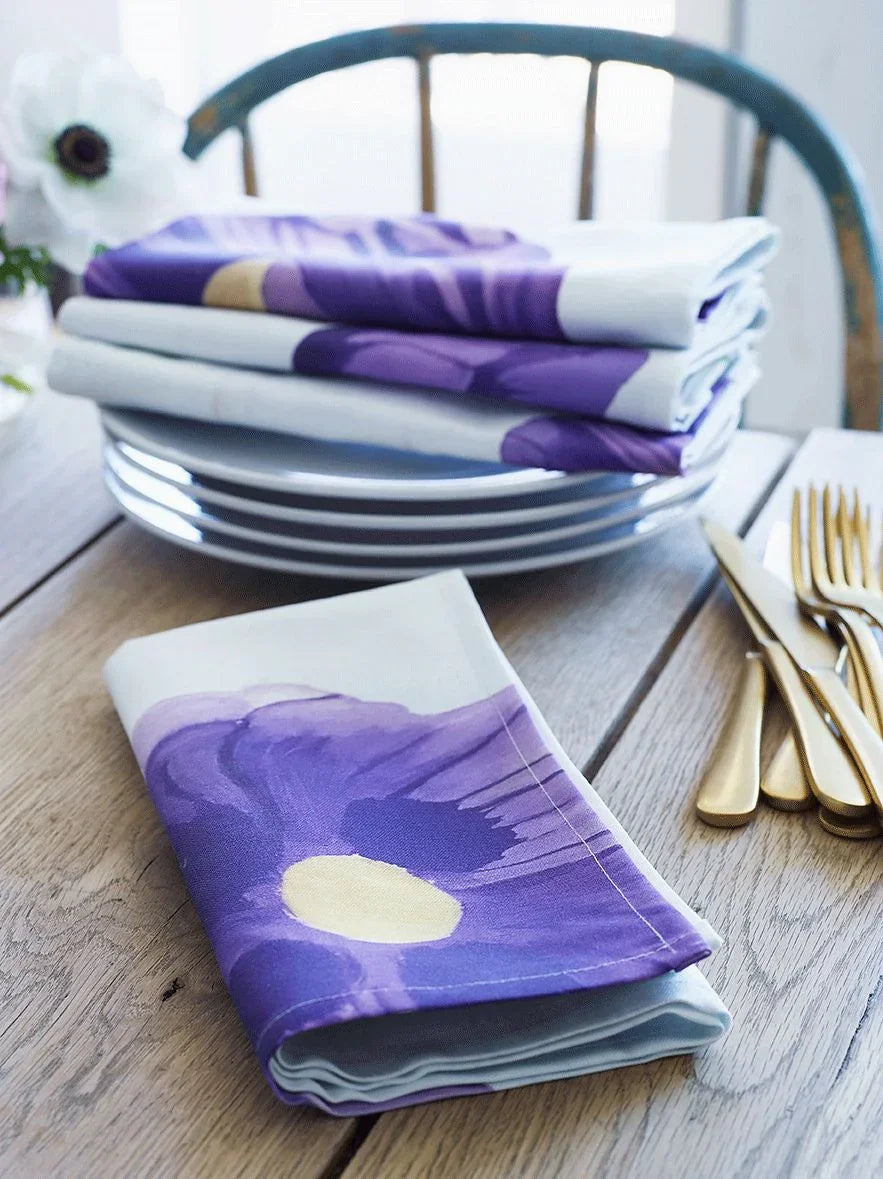 Folded purple poppies napkins on wooden table with gold cutlery and white plates