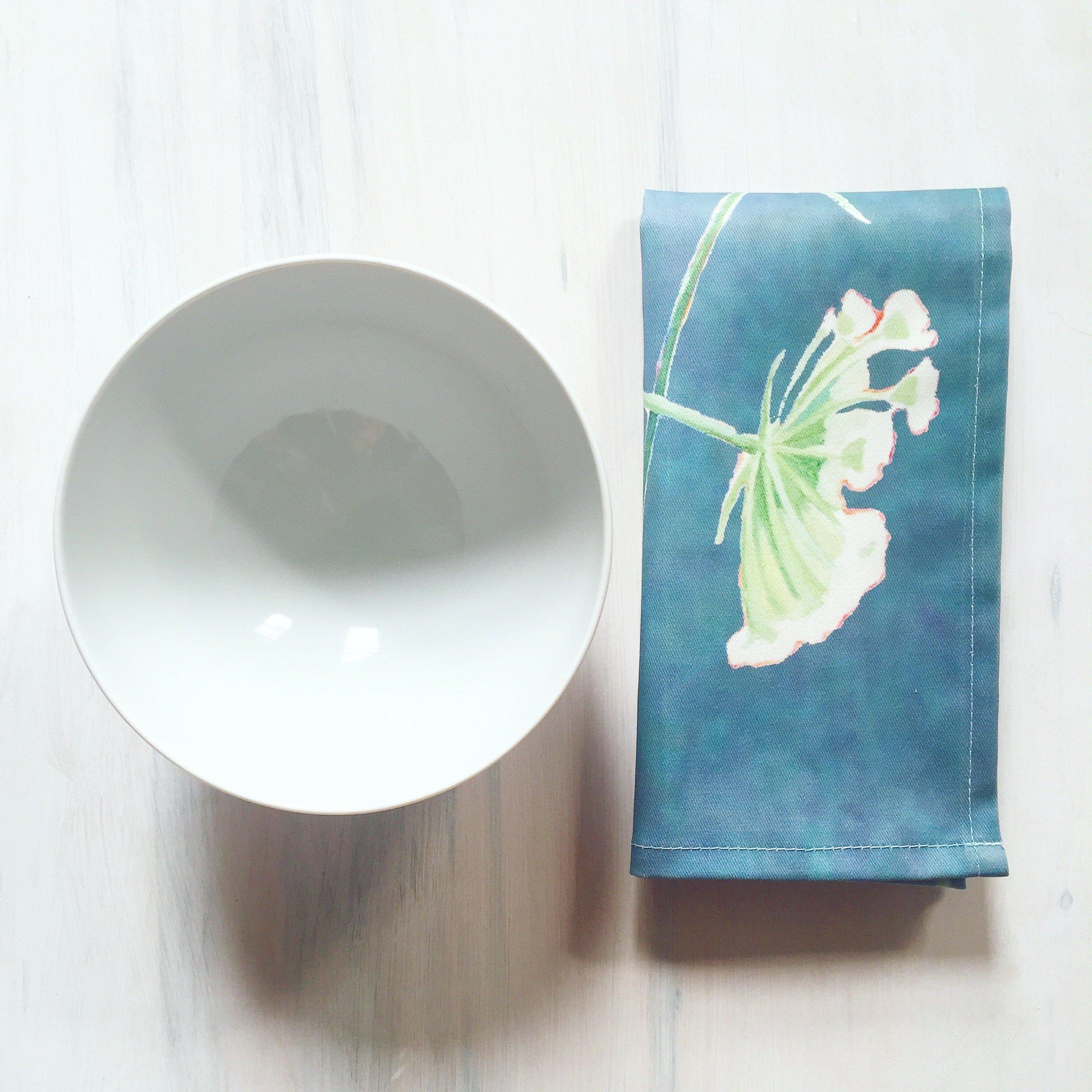 White ceramic bowl next to folded teal napkin with Queen Anne's lace flower design