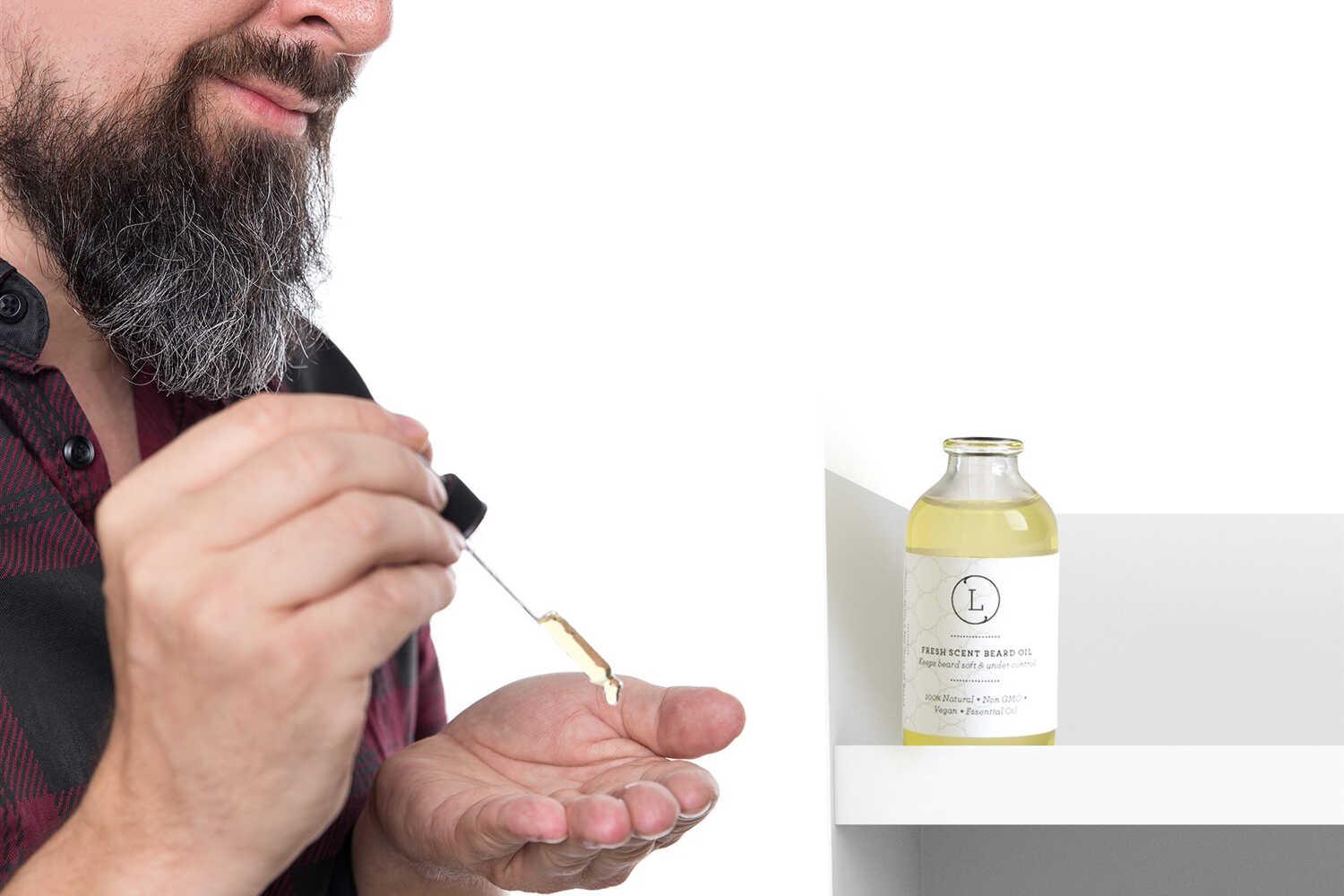 Bearded man applying fresh scent beard oil with dropper, natural beard care product on white shelf