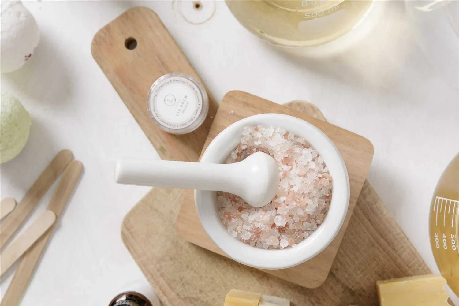 Mortar with pink Himalayan bath salt and pestle on wooden cutting boards with spa accessories