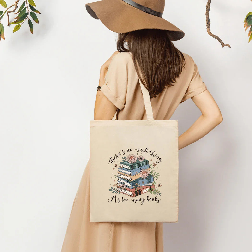 Woman in beige dress and hat holding tote bag with books and floral print reading "There's no such thing as too many books"