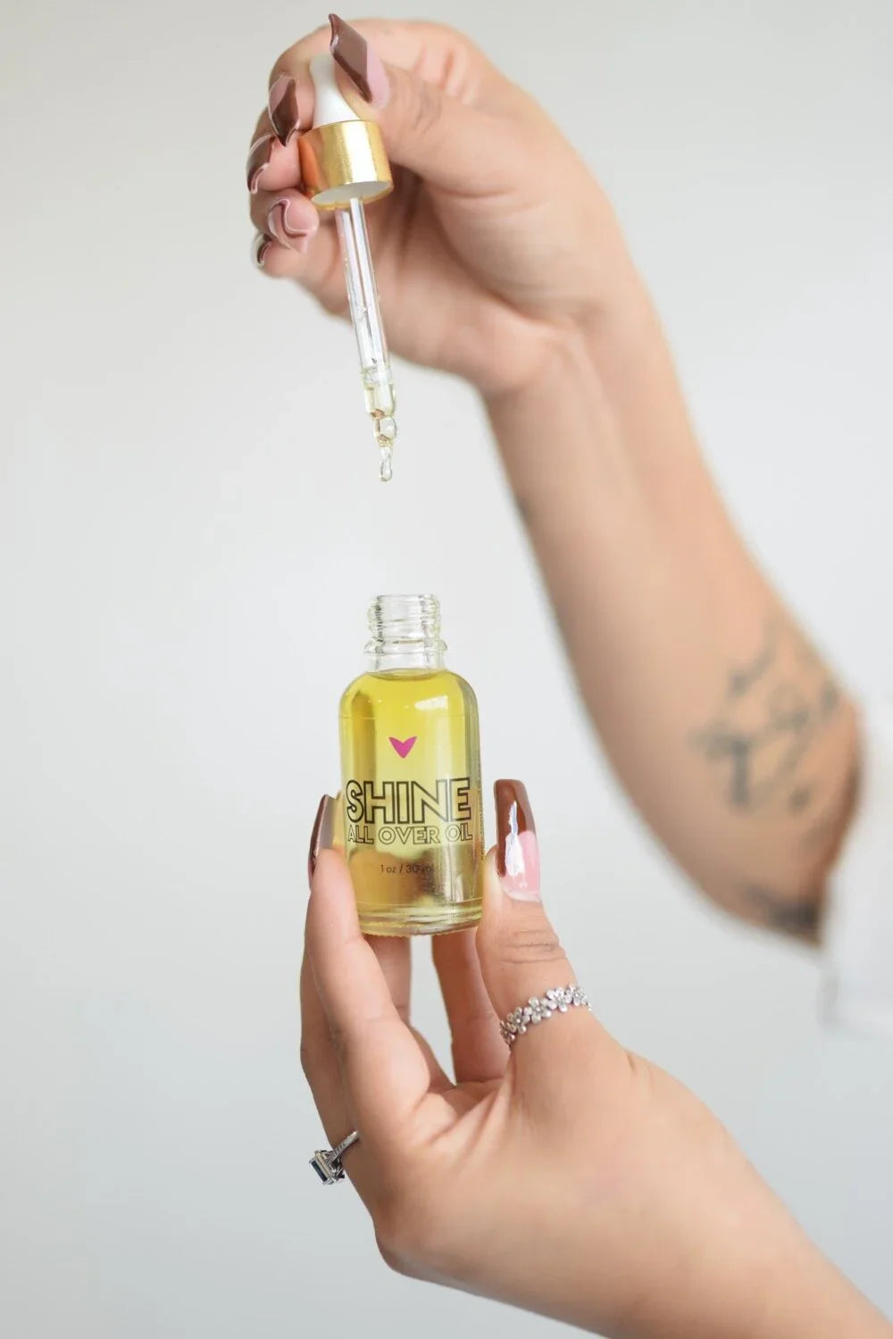Hand holding Shine All Over Oil dropper bottle, eco-friendly beauty product at Qu!rk Boutique
