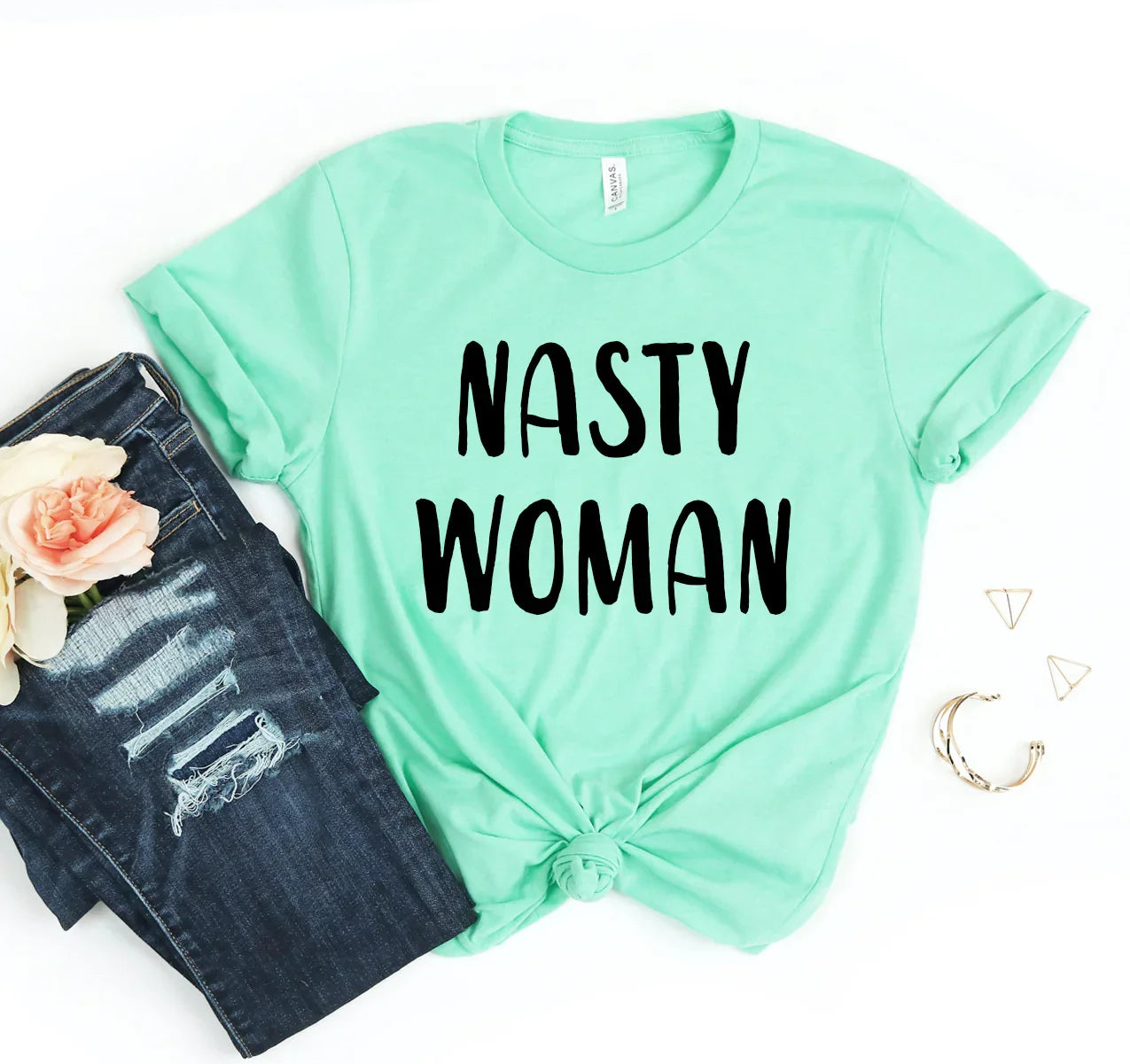 Mint green t-shirt with black text 'NASTY WOMAN', styled with ripped dark blue jeans and gold jewelry