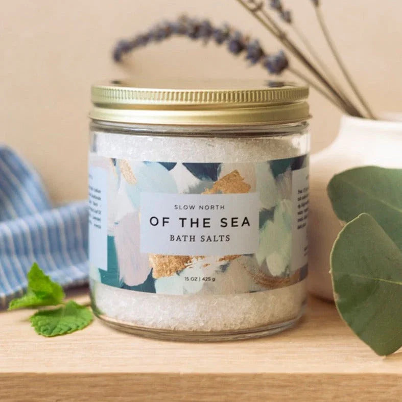 Jar of Slow North Of The Sea bath salts with colorful label on wooden surface with greenery