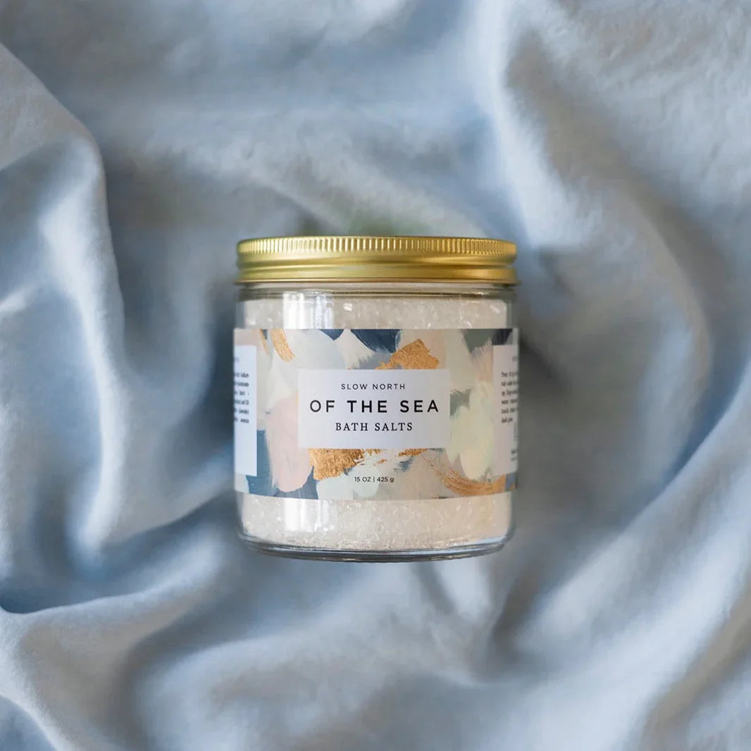 Jar of Slow North Of The Sea bath salts with gold lid on soft light blue fabric