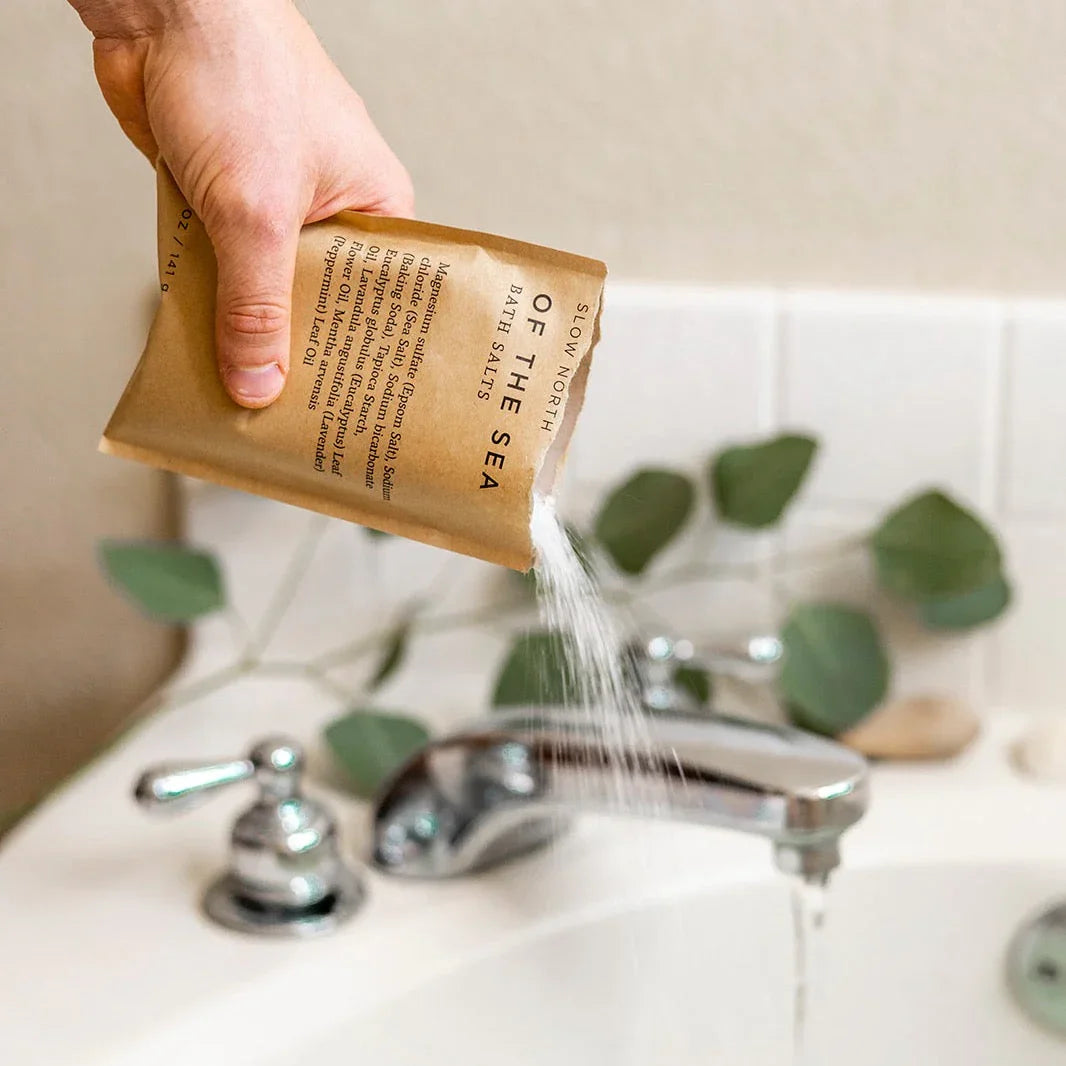 Hand pouring Slow North Of The Sea bath salts into a white tub at Qu!rk Boutique