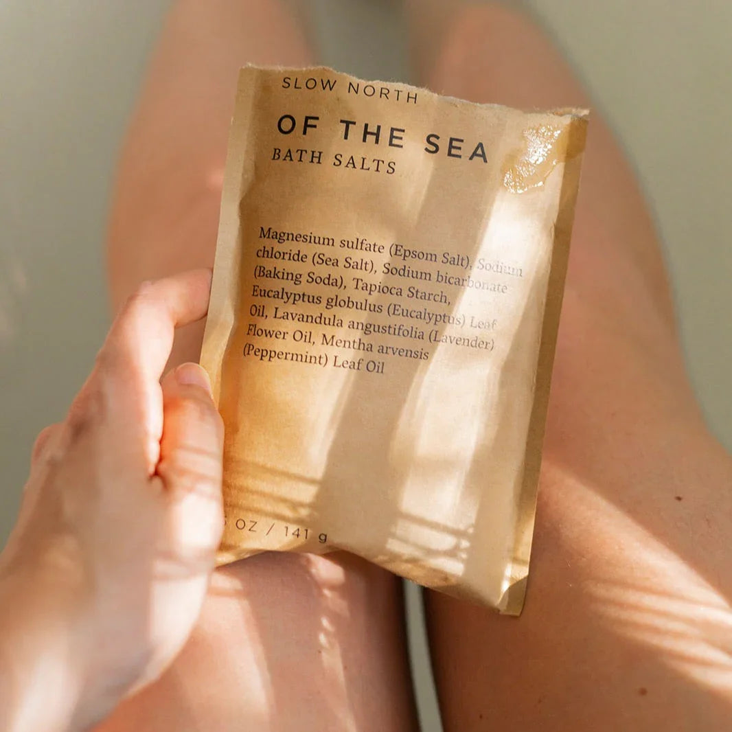Hand holding Slow North Of The Sea bath salts pouch over legs in a relaxing bath