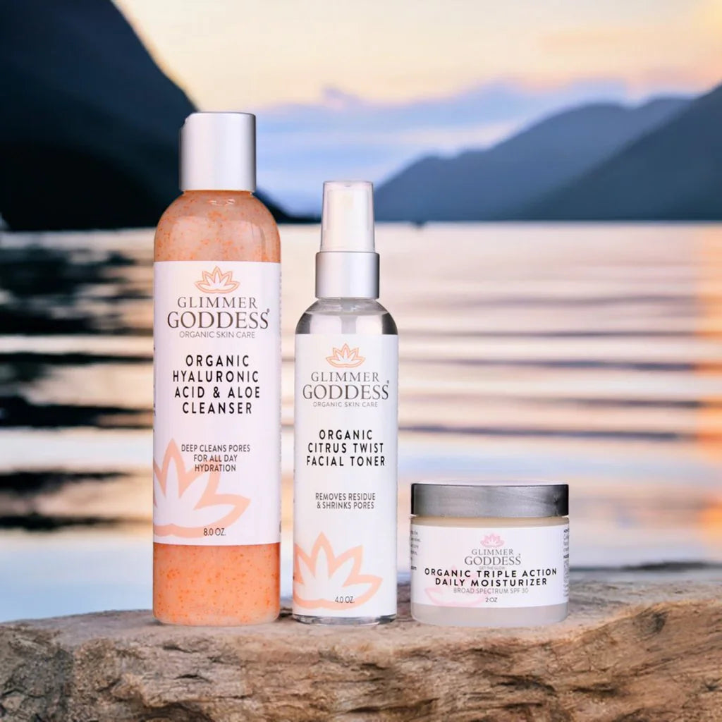 Glimmer Goddess organic anti-aging skin care kit with cleanser, toner, and moisturizer on rock by water