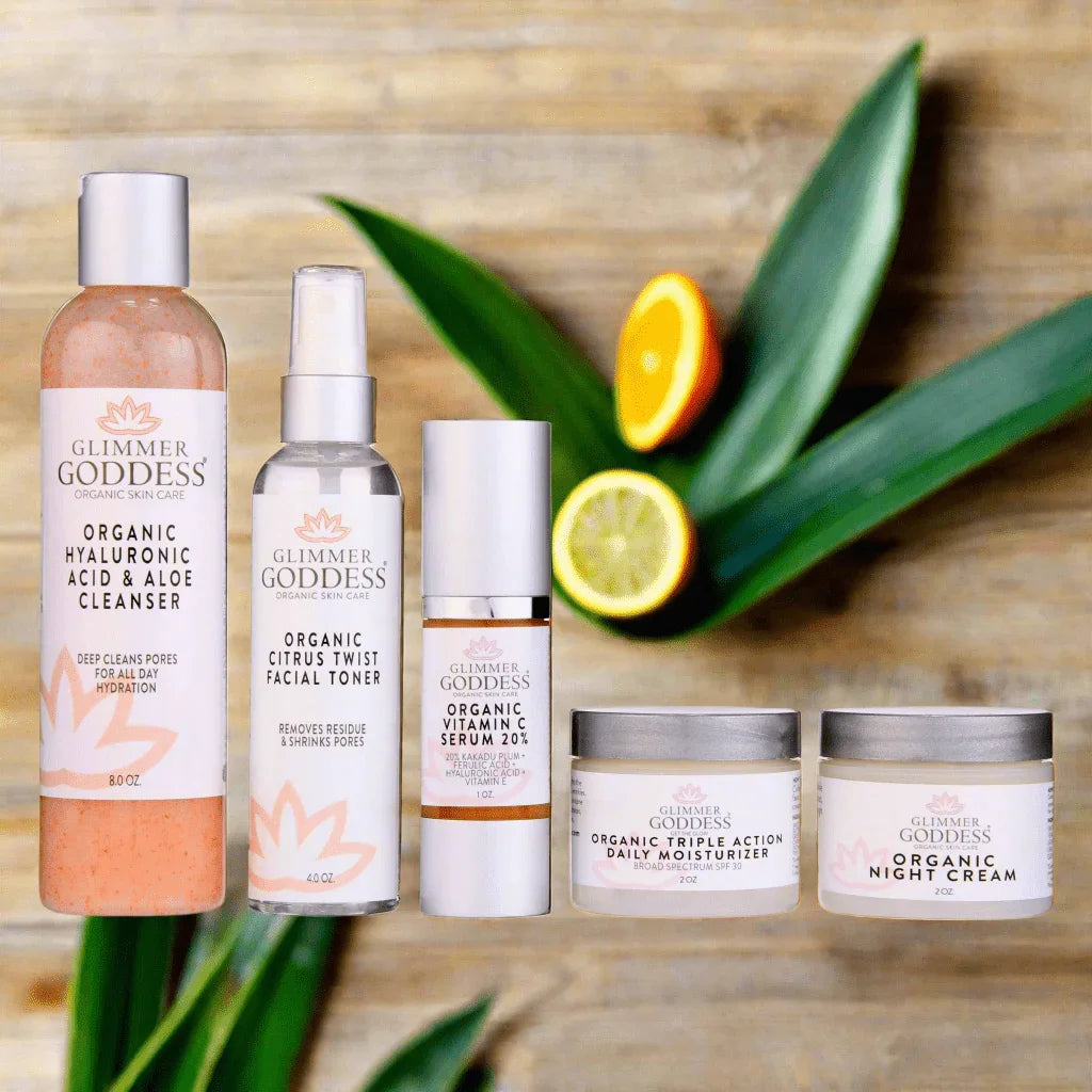 Glimmer Goddess organic skincare set with cleanser, facial toner, vitamin C serum, moisturizer, and night cream on wood