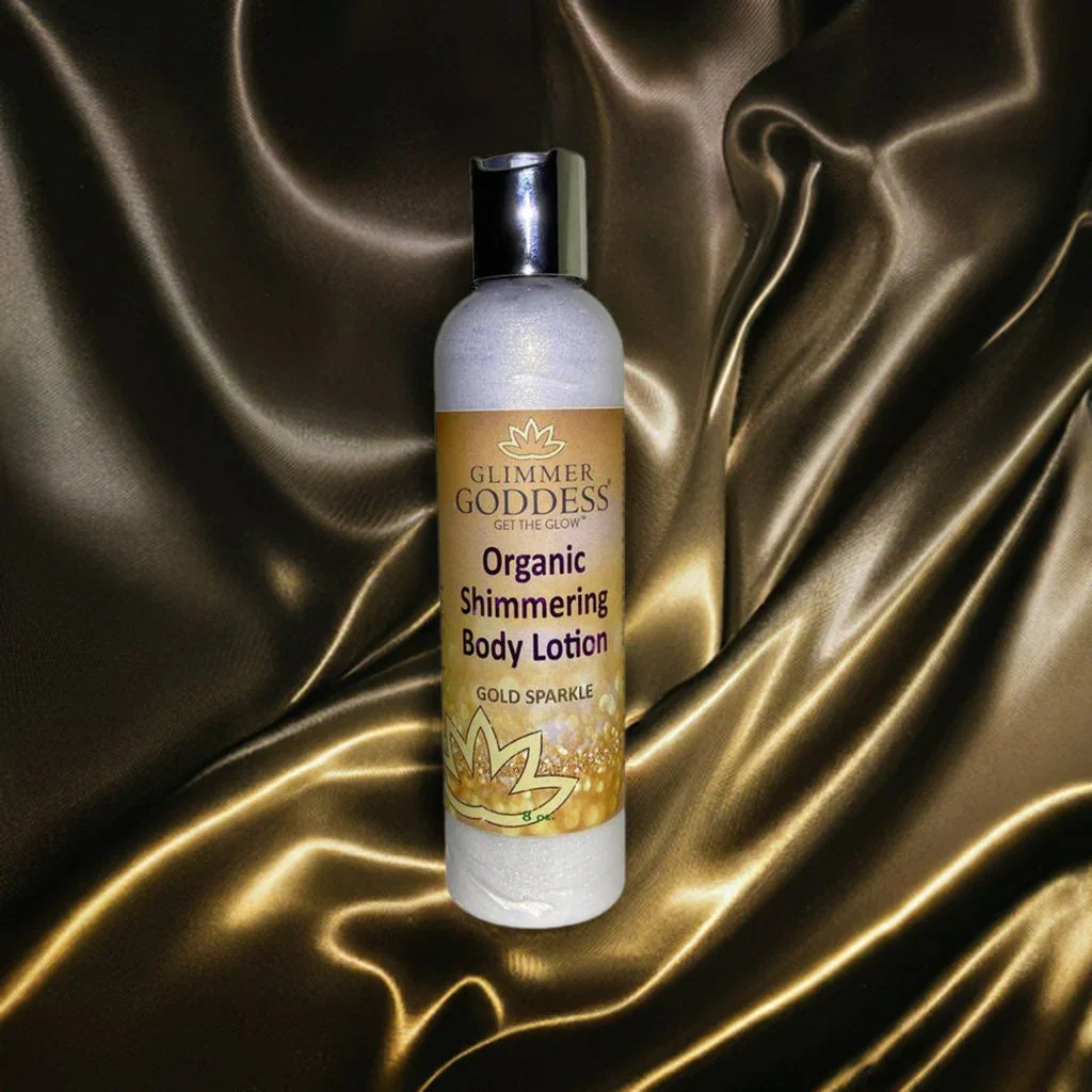 Glimmer Goddess organic shimmering body lotion with gold sparkle on luxe golden fabric