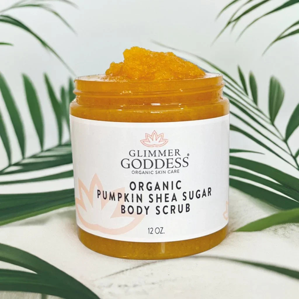 Open jar of Glimmer Goddess organic pumpkin shea sugar body scrub on white surface with green leaves
