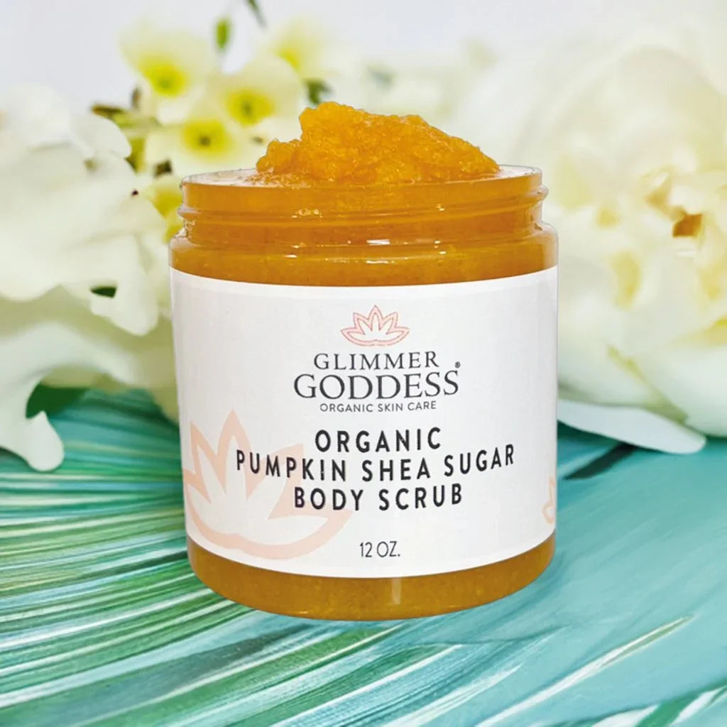 Glimmer Goddess organic pumpkin shea sugar body scrub jar on green leaf with white flowers