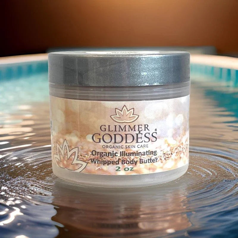 Glimmer Goddess Organic Illuminating Whipped Body Butter 2 oz jar on water surface with shimmering background