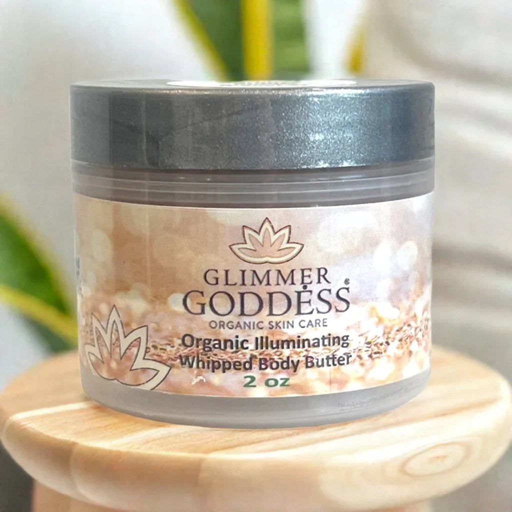 Glimmer Goddess organic illuminating whipped body butter 2 oz jar on wooden surface with blurred green background