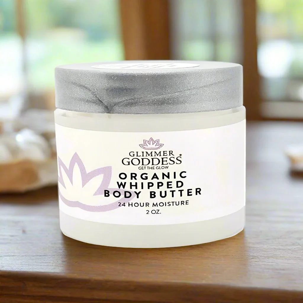 Glimmer Goddess organic whipped body butter 2 oz jar on wooden surface with blurred background