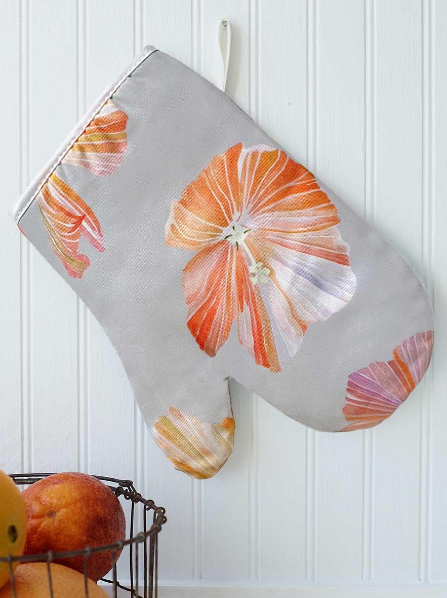 Gray oven mitt with large orange hibiscus flower print hanging on white beadboard wall