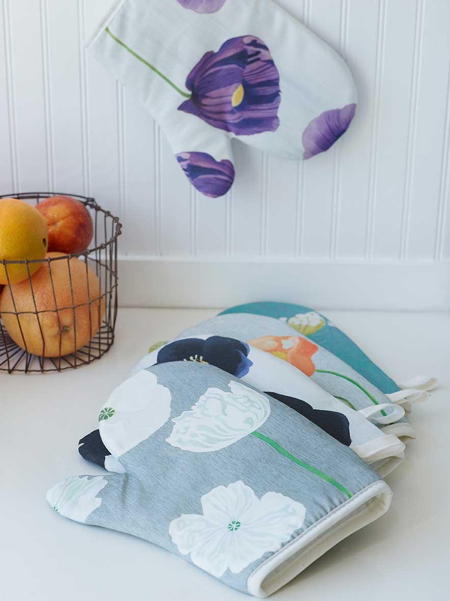 Colorful floral print oven mitts on white kitchen counter with wire basket of fruit
