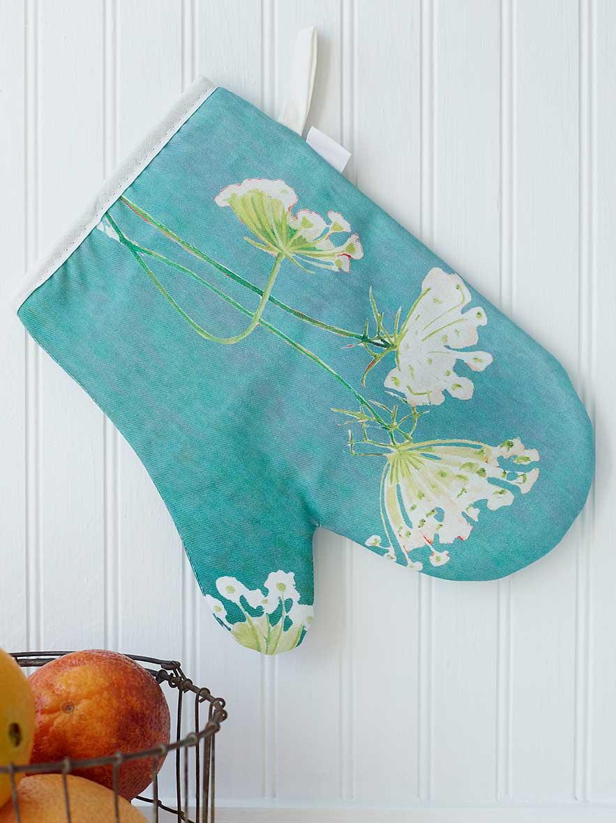 Teal oven mitt with white Queen Anne’s lace flowers hanging on white paneled wall