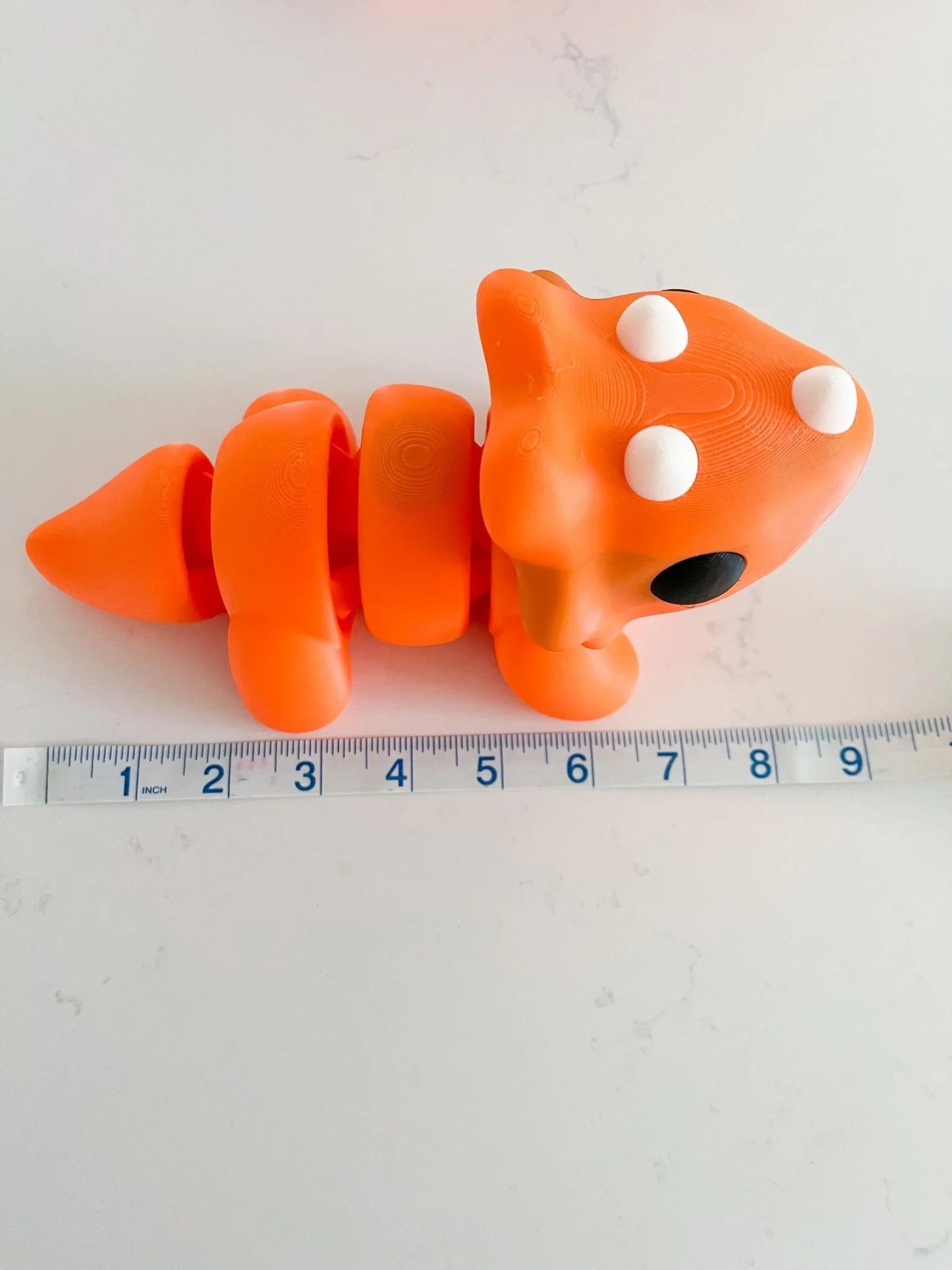 Oversized chunky orange triceratops toy with white spots, next to a ruler on white background