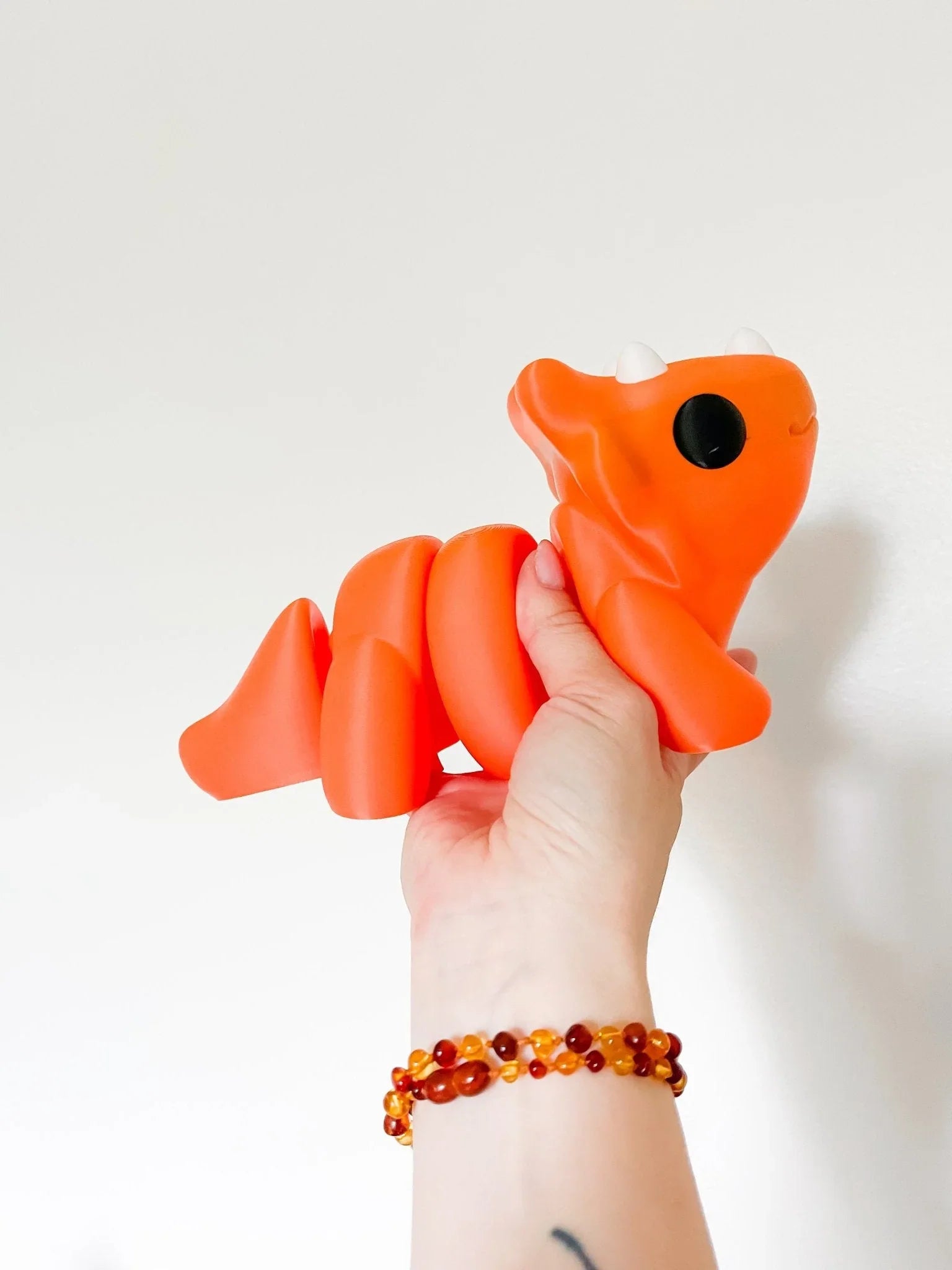 Hand holding oversized chunky orange triceratops toy against a white background