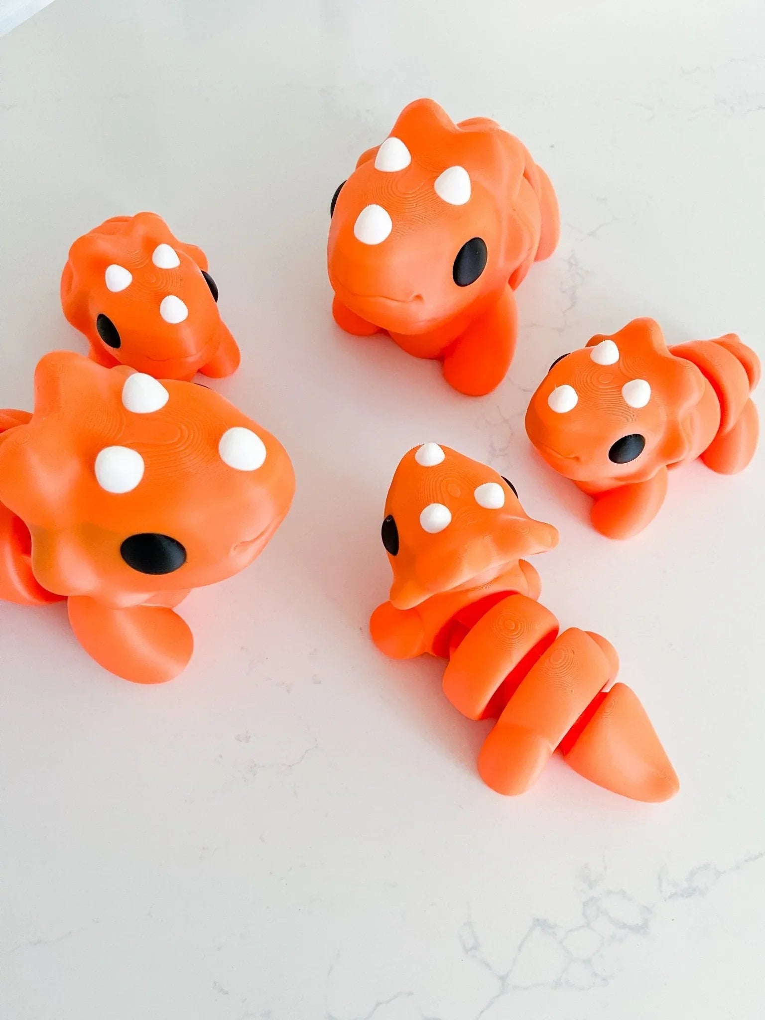 Oversized chunky orange triceratops toys with white horns on a white surface, quirky gift idea