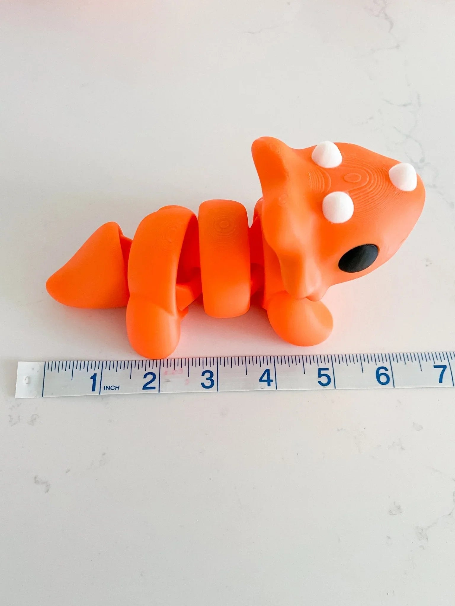 Oversized chunky orange triceratops toy on white surface with ruler for scale, Qu!rk Boutique