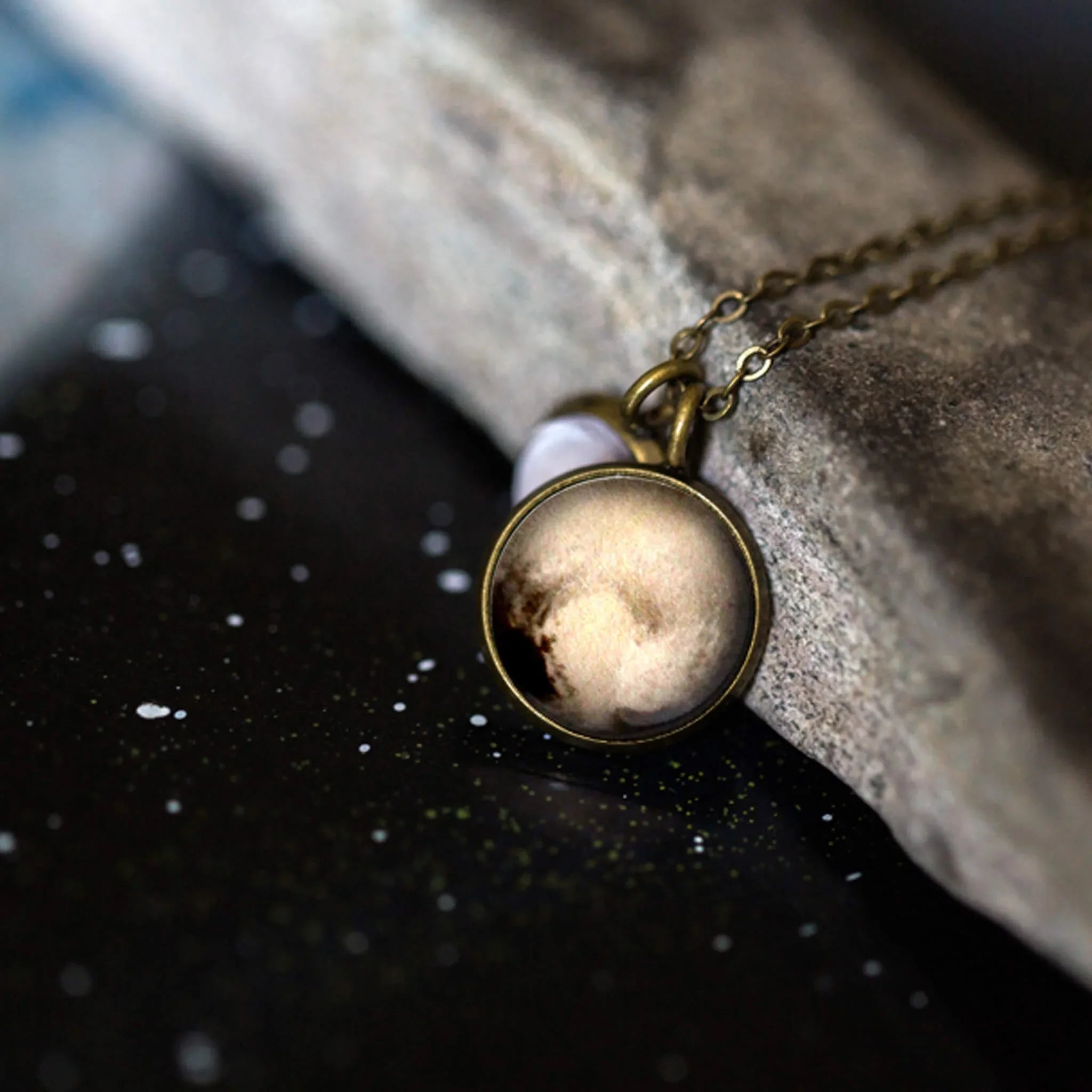 Brass planet pendant necklace on cosmic speckled surface, Qu!rk boutique artist jewelry
