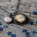 Cosmic moon phase pendant necklace on rustic wood with blue star confetti, Qu!rk Boutique