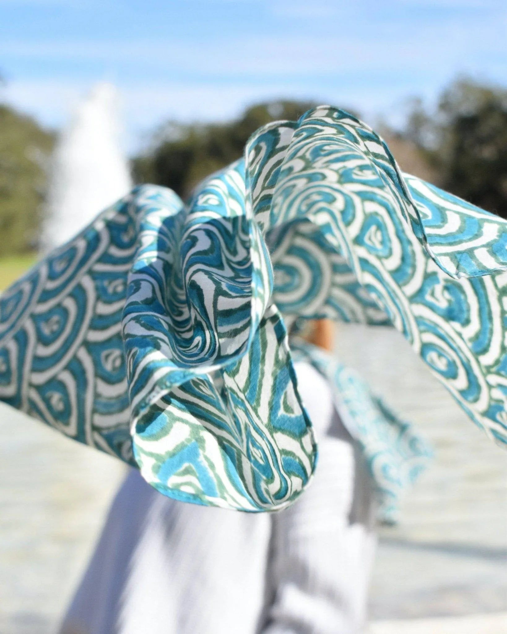 Teal and white artist-designed scarf with peacock pattern blowing outdoors, Qu!rk Boutique