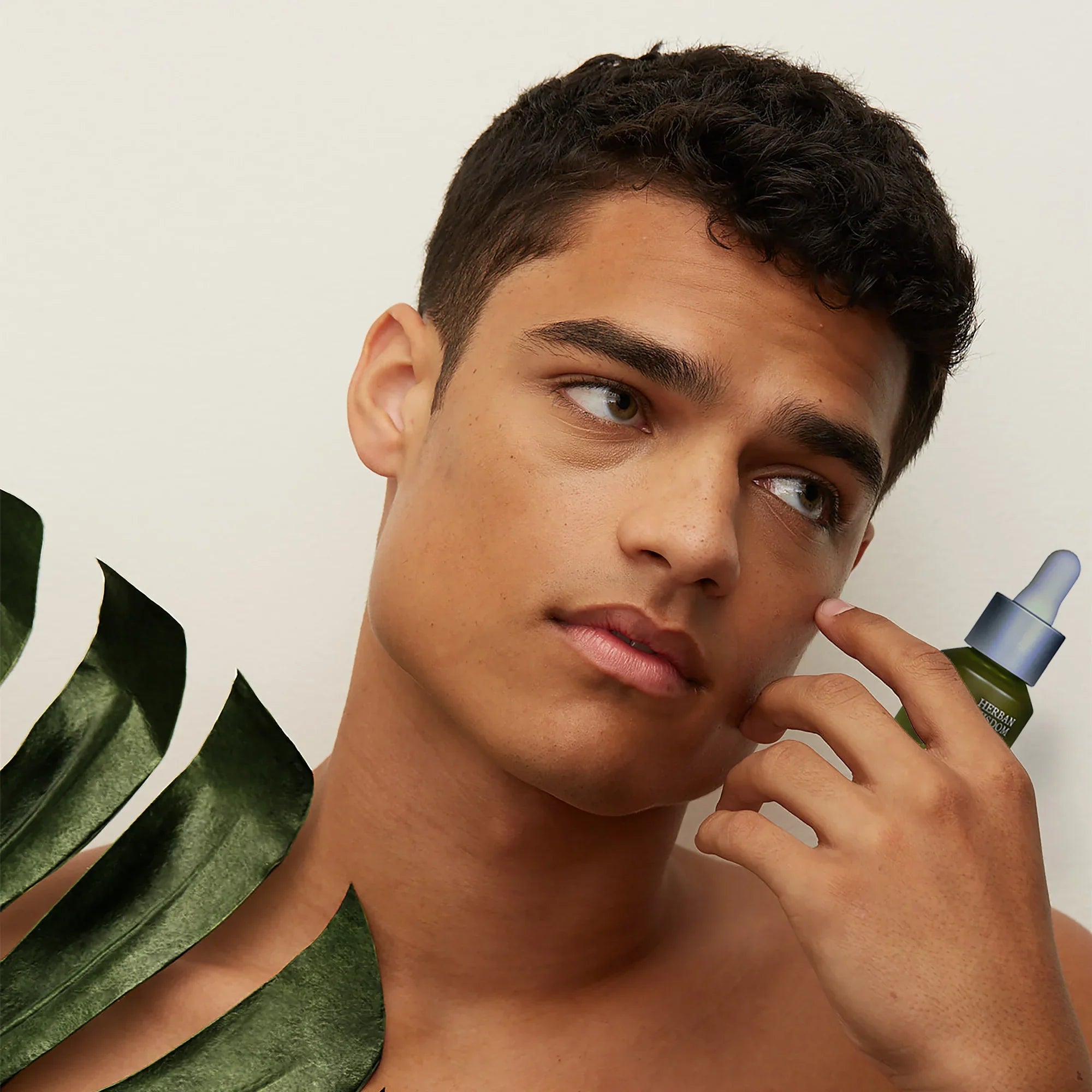 Young man applying green serum to face with dropper, botanical skincare concept, Qu!rk Boutique