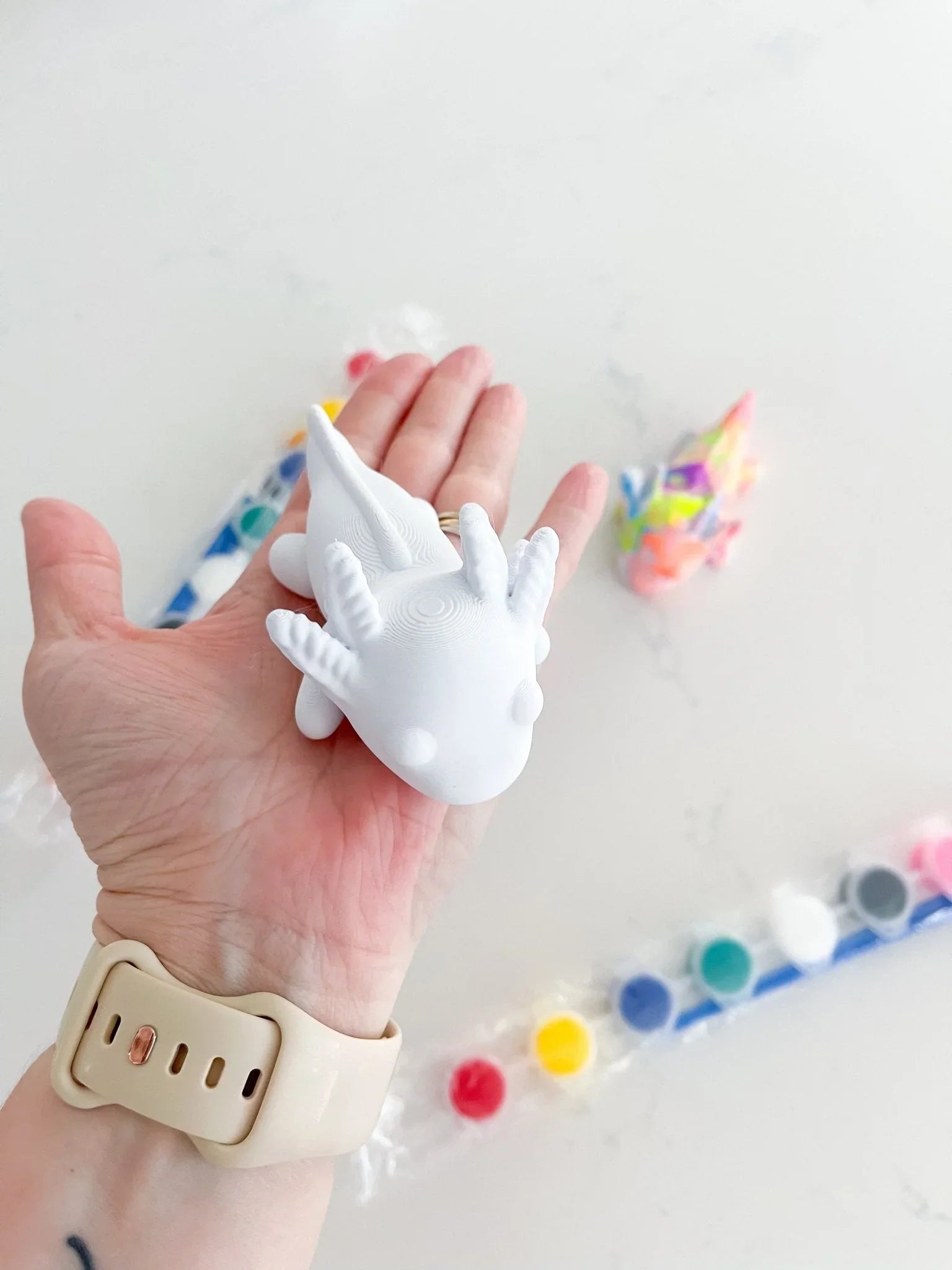 Hand holding white axolotl figurine with paint kit, Qu!rk Boutique craft gift