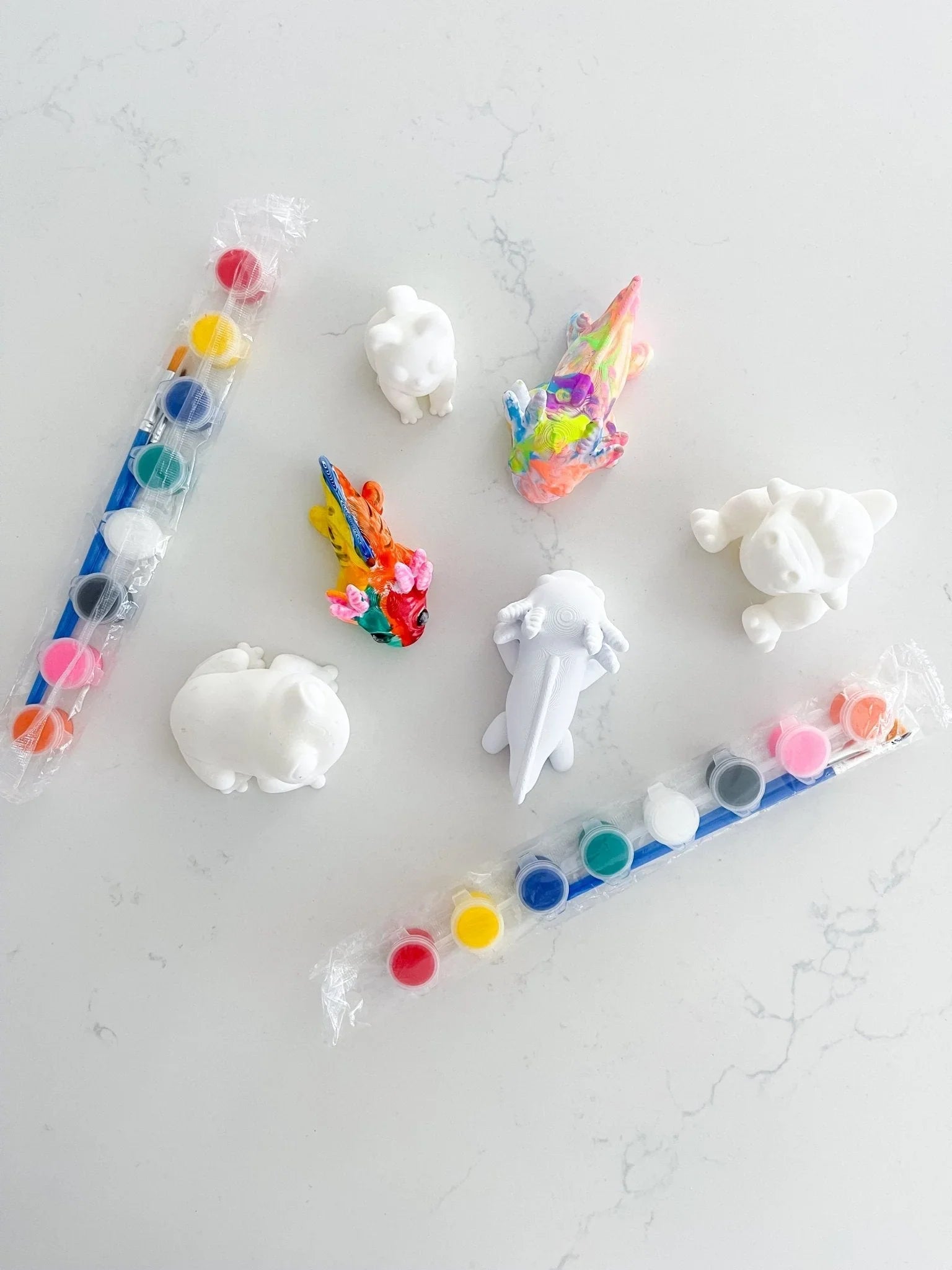 Pick and paint kit with unpainted animal figurines, colorful paints, and brushes on white background