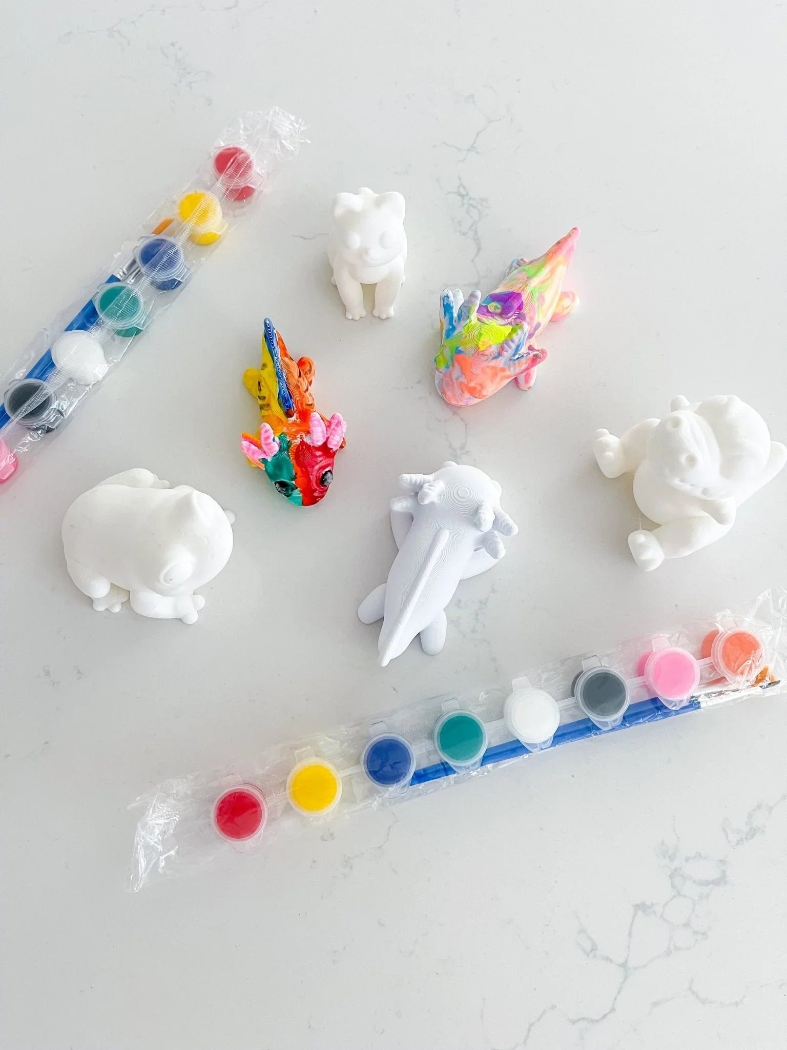 DIY pick and paint kit with unpainted animal figurines, paintbrushes, and colorful paints on white table