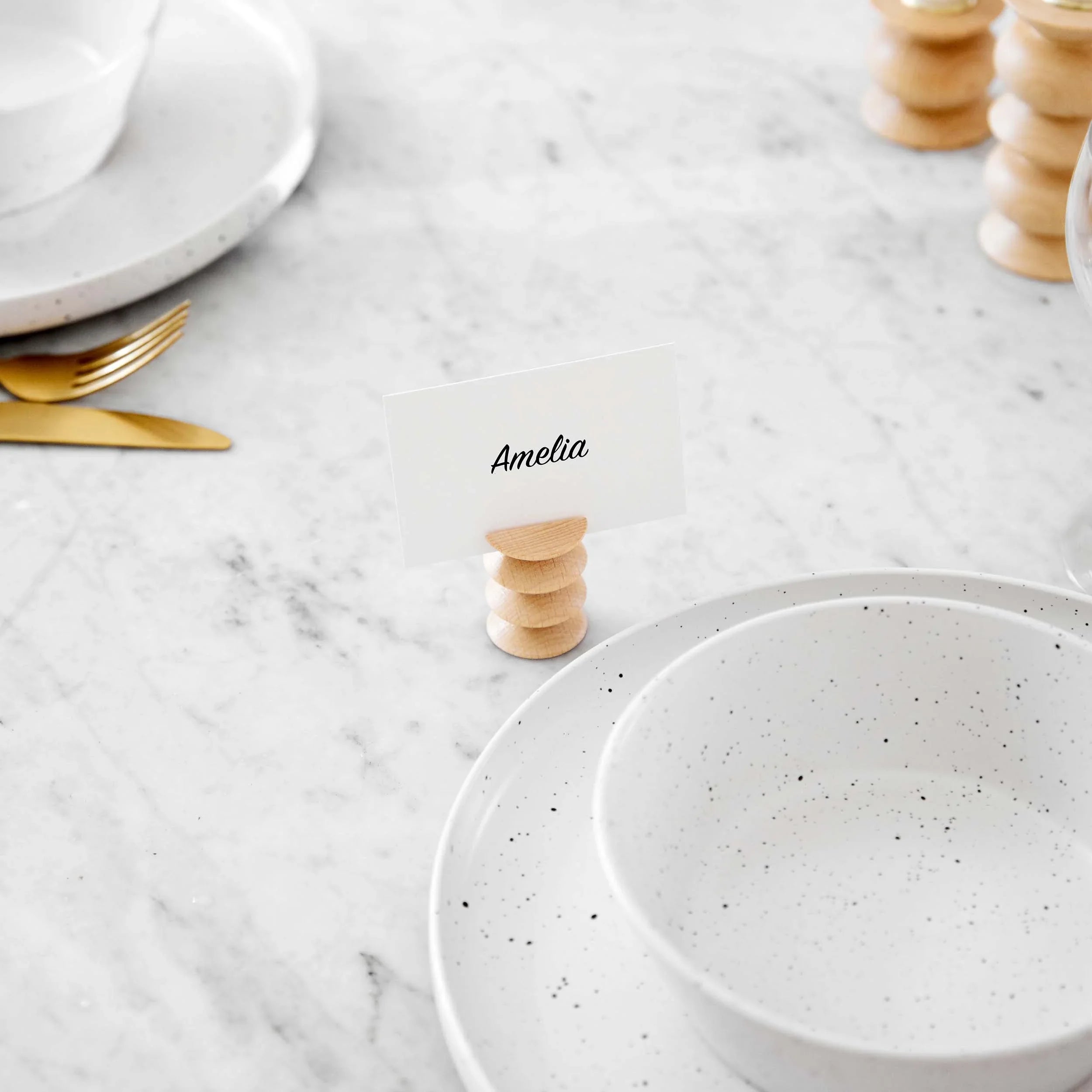 Minimalist wooden card holder with name card on marble table, beside speckled dishware