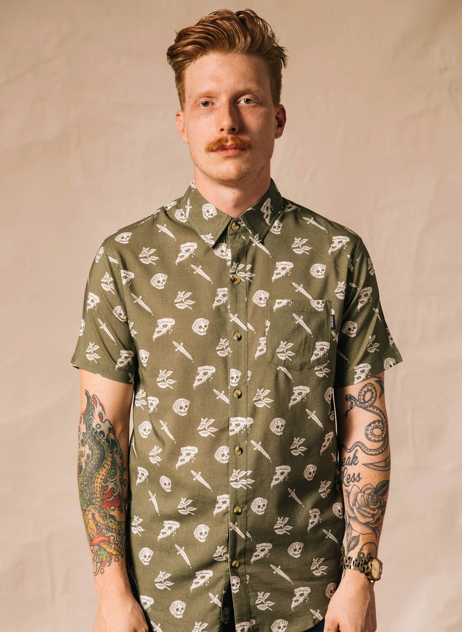Man wearing olive green button-up shirt with white pizza, skull, and dagger print, Qu!rk Boutique