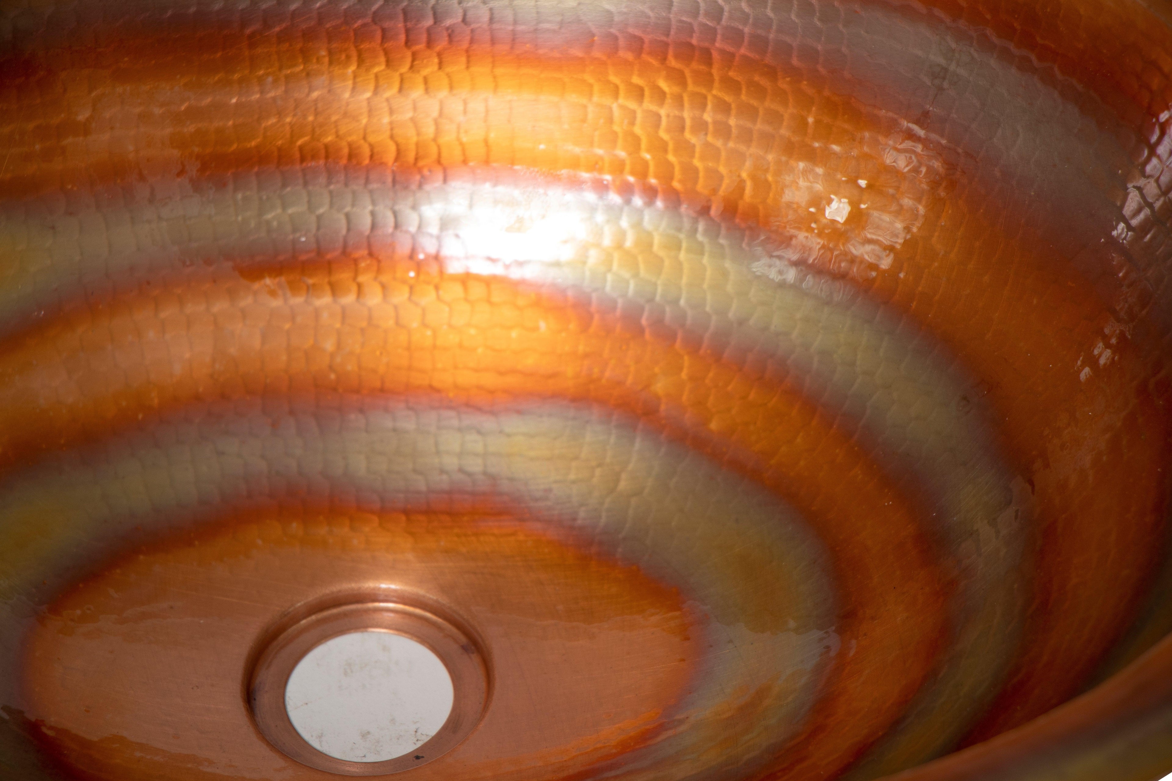 Handcrafted hammered copper sink with orange and gold swirl pattern, artisan home decor