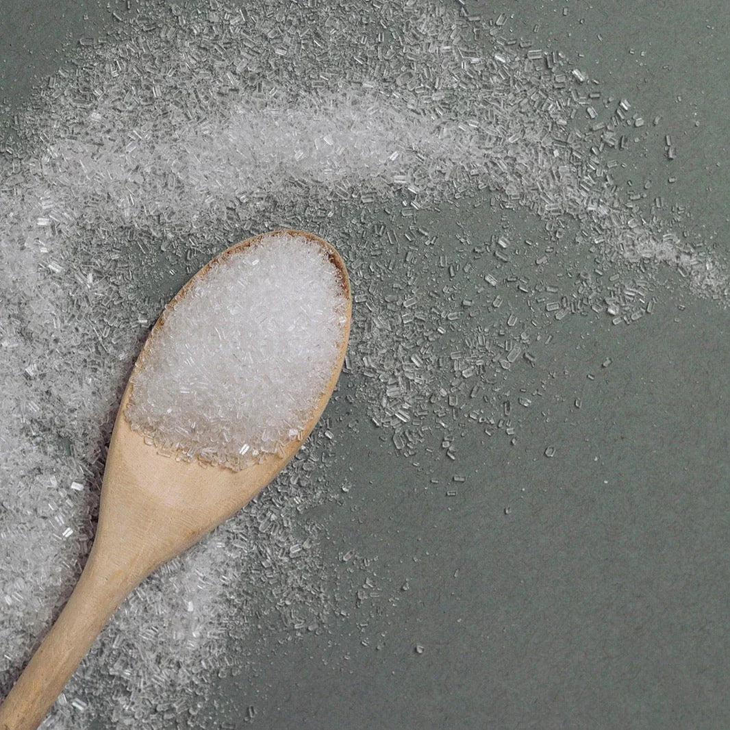 Wooden spoon filled with coarse white bath salt crystals on gray surface with scattered salts