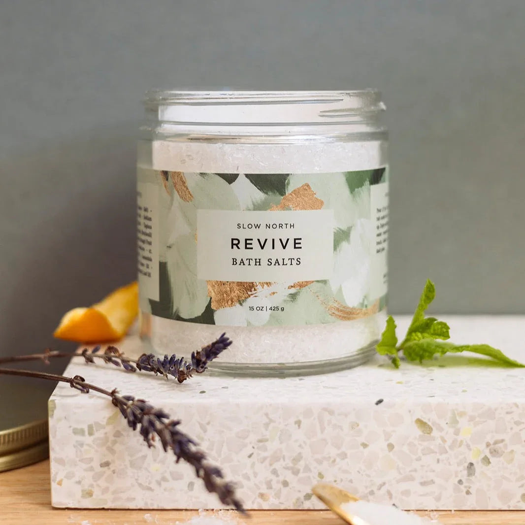 Jar of Slow North Revive bath salts on terrazzo surface with lavender, mint, and orange peel