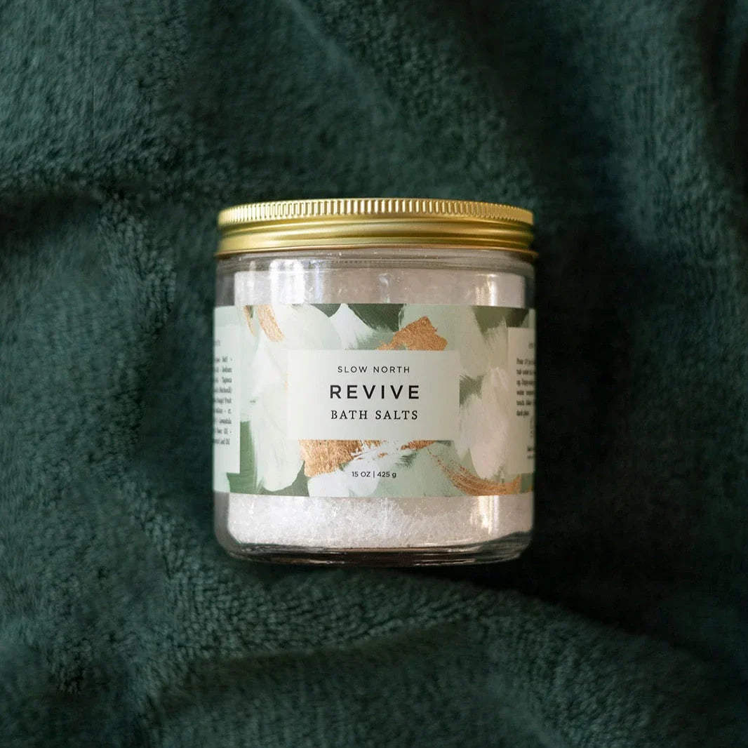 Slow North Revive bath salts jar with gold lid on dark green textured fabric