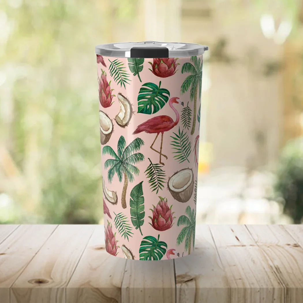 Pink travel tumbler with tropical flamingo, coconut, palm leaves, and dragon fruit design on wooden table