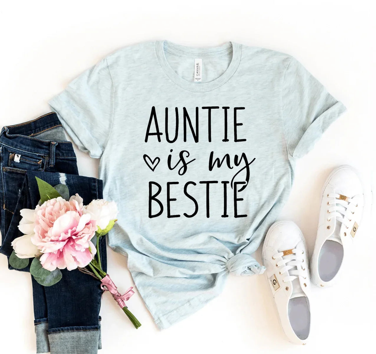 Light blue t-shirt with 'Auntie is my bestie' text laid out with dark jeans, pink flowers, and white sneakers